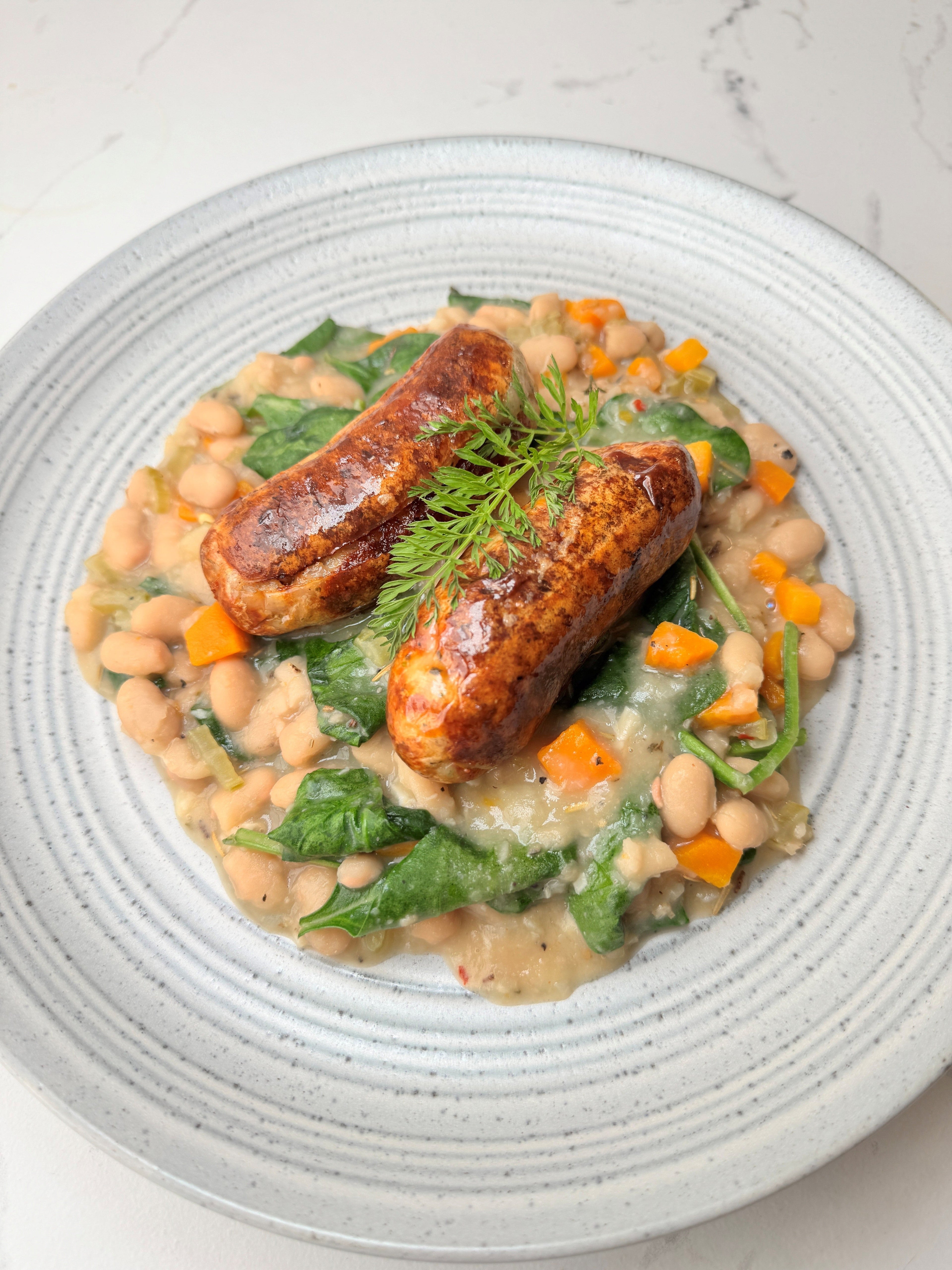 Two Herb Fed lemon and garlic sausages on a bed of white beans | Herb Fed Poultry
