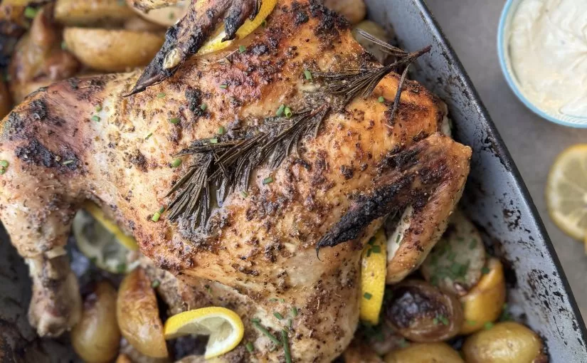A Herb Fed Spatchcock Chicken served on a tray with Potatoes, lemons and fresh herbs | Herb Fed Poultry