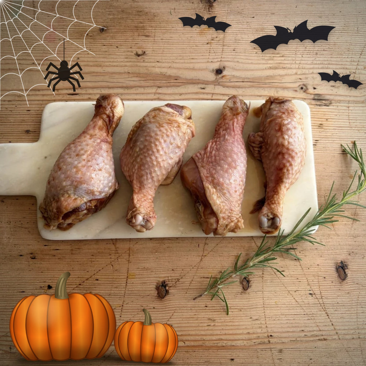 Herb Fed Drumsticks marinated in a pomegranate molasses sauce laid on a white board on a wooden table. Ideal for a Halloween feast.