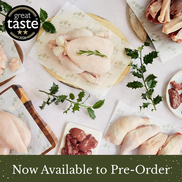 Raw herb fed chicken box including a whole chicken, chicken legs, carcass, chicken liver, chicken fillet, diced chicken and chicken giblets arranged on parchment paper with herbs and wooden boards. A black circular '2 star great taste 2026' award badge appears in the top-left, and a green banner at the bottom reads 'Now Available to Pre-Order'.