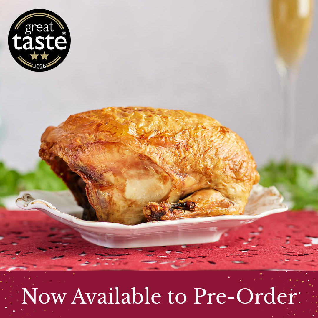 A roasted herb fed Christmas Rooster Crown on a white plate, set on a red patterned tablecloth with a blurred glass of champagne in the background. A 'great taste 2026' award badge is in the top-left corner, and a 'Now Available to Pre-Order' banner is at the bottom.