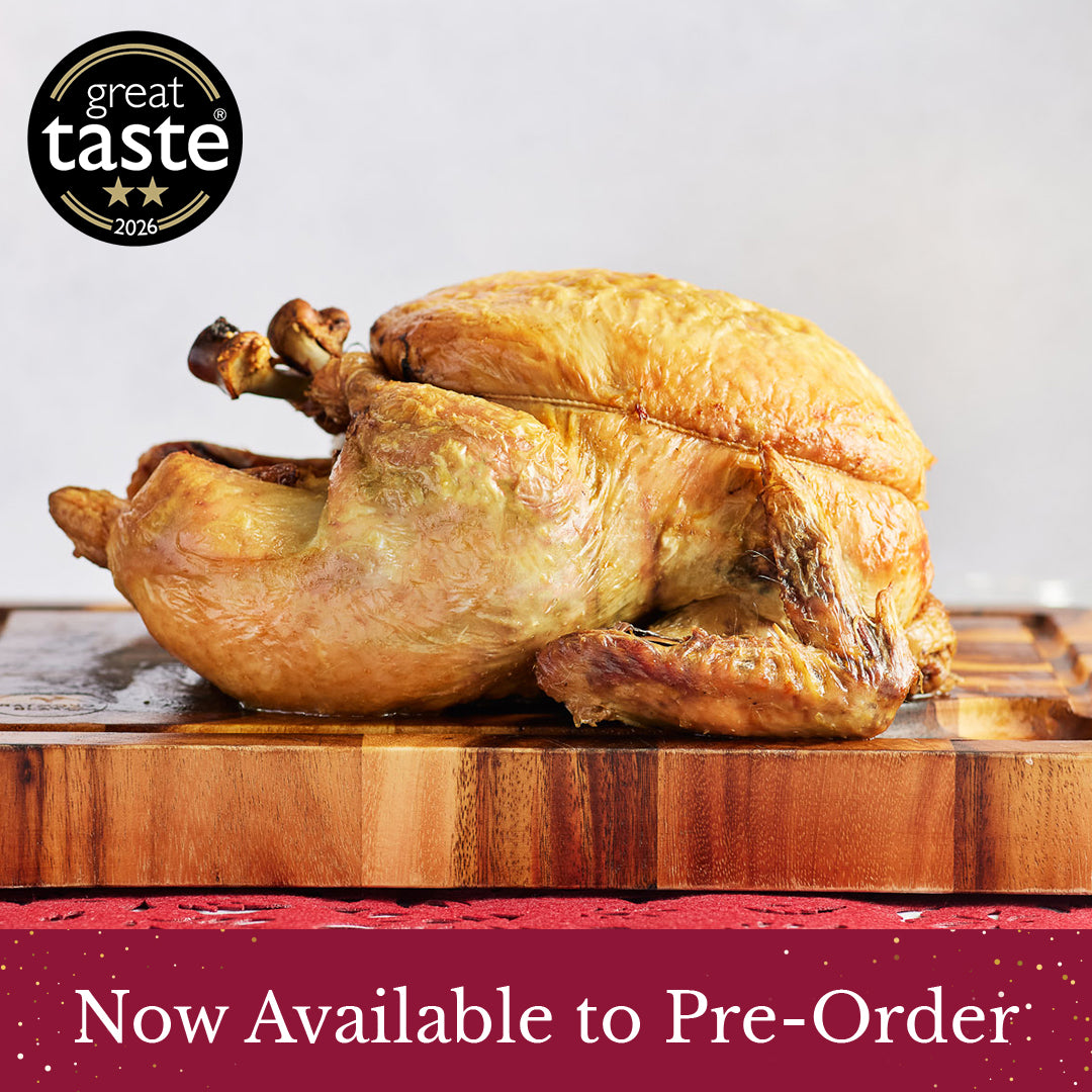 A whole roasted herb fed Christmas Rooster with crispy golden-brown skin displayed on a wooden cutting board, with a '2 star great taste 2026' award badge in the top-left corner and a red banner at the bottom reading 'Now Available to Pre-Order'.
