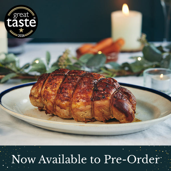 A roasted herb fed turkey breast joint with a glossy, golden-brown glaze served on a white plate with a dark rim, set against a softly blurred festive dining background with candles, carrots, and greenery. A 'great taste 2026' award badge appears in the top-left corner, and a dark banner at the bottom reads 'Now Available to Pre-Order'.