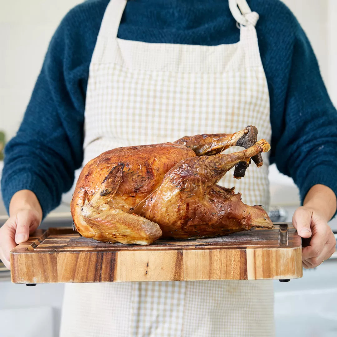 A roast turkey on a wooden board being held by someone | Herb Fed Poultry