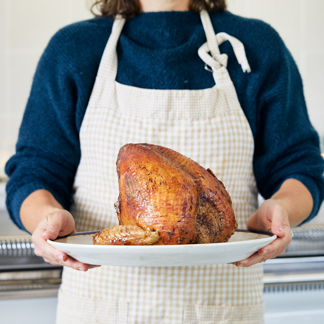 A person holding a roast turkey crown on a plate | Herb Fed Poultry