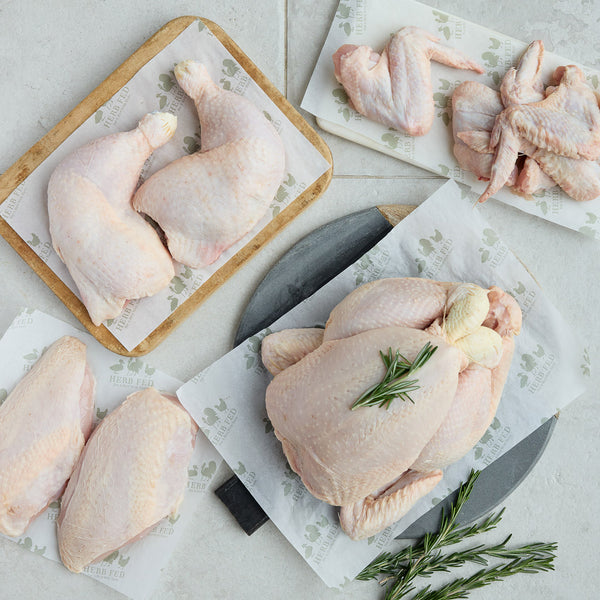 Raw chicken pieces on cutting boards with a knife and rosemary on a light background | Herb Fed Poultry