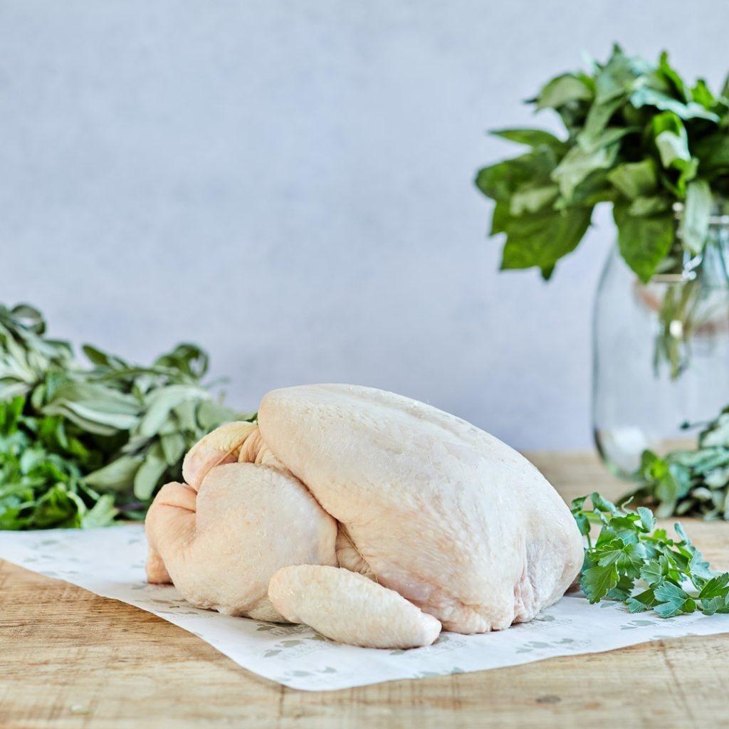 A dressed chicken and herbs on a table (not cooked)